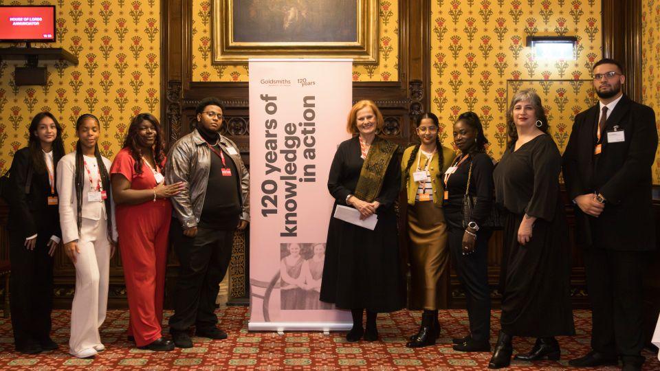 Group of students and staff (nine in total) pose by 120 year Knowledge in Action banner