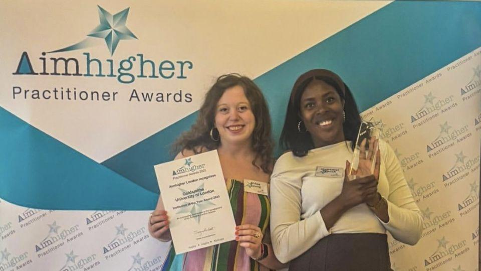 Chloe Young and Christabel Yeboah standing in front of an Aimhiger Practitioner Awards background holding the certificate and trophy
