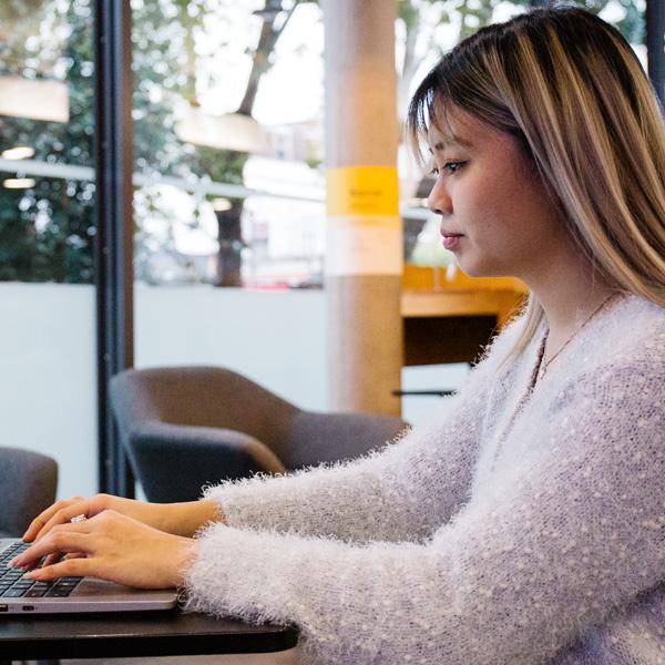 A student working on a laptop in a modern university library. 