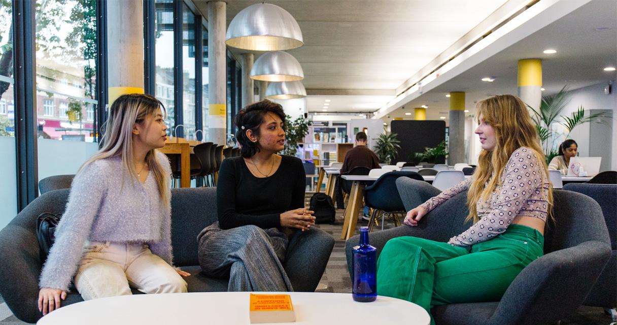 Three students sit in a social space in a modern university library
