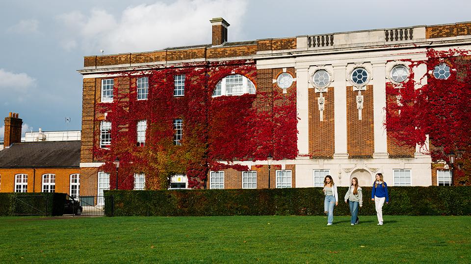 Three students walking on green grass, with university building in the background.