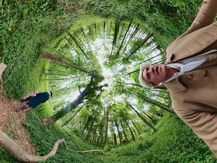 Surreal fish eye image of forest and man with white wig on looking startled.
