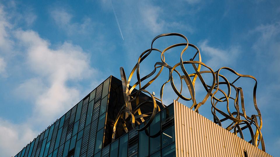 Modern university building with squiggle sculpture on the roof, blue skies in the background.