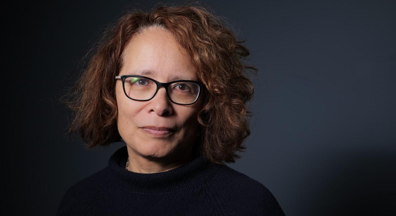 Portrait photograph of Professor Bridget Anderson, wearing a dark top in front of a deep blue blackground