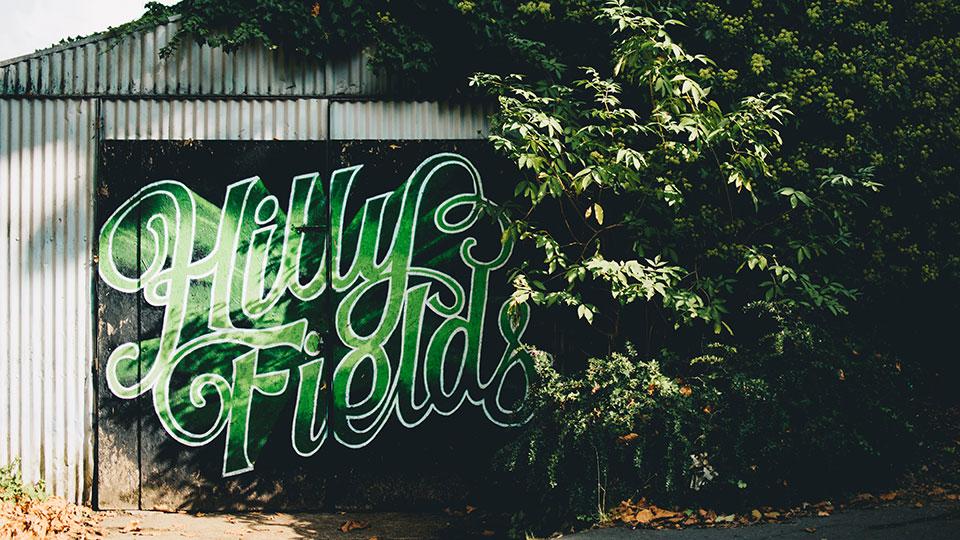 'Hilly Fields' painted in a green cursive font on a wall