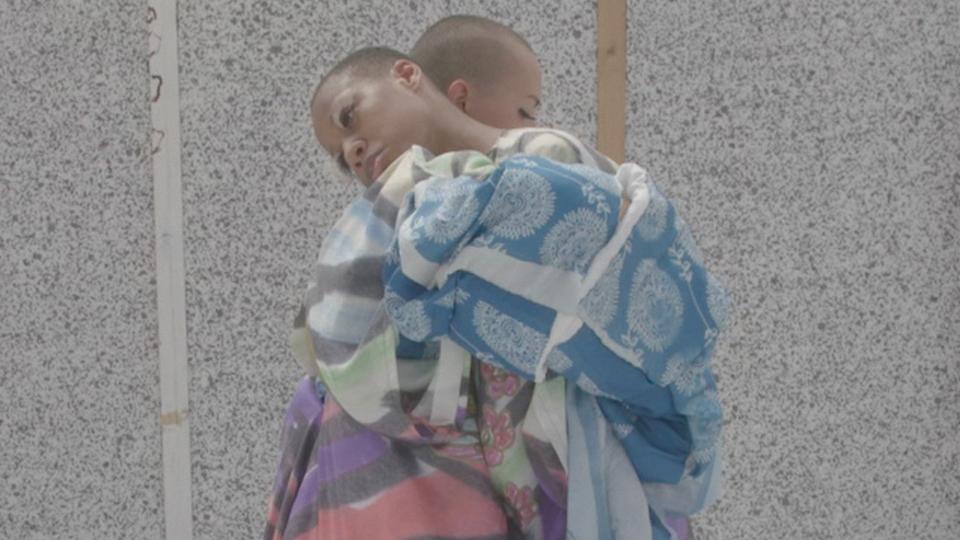 Two figures in elaborate coloured gowns embrace