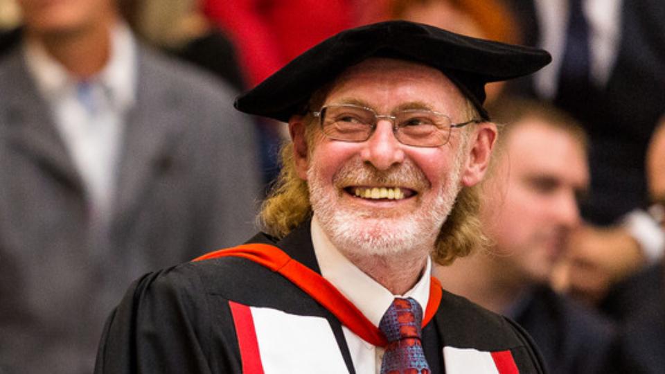 Bearded man, seated, smiling in ceremonial dress
