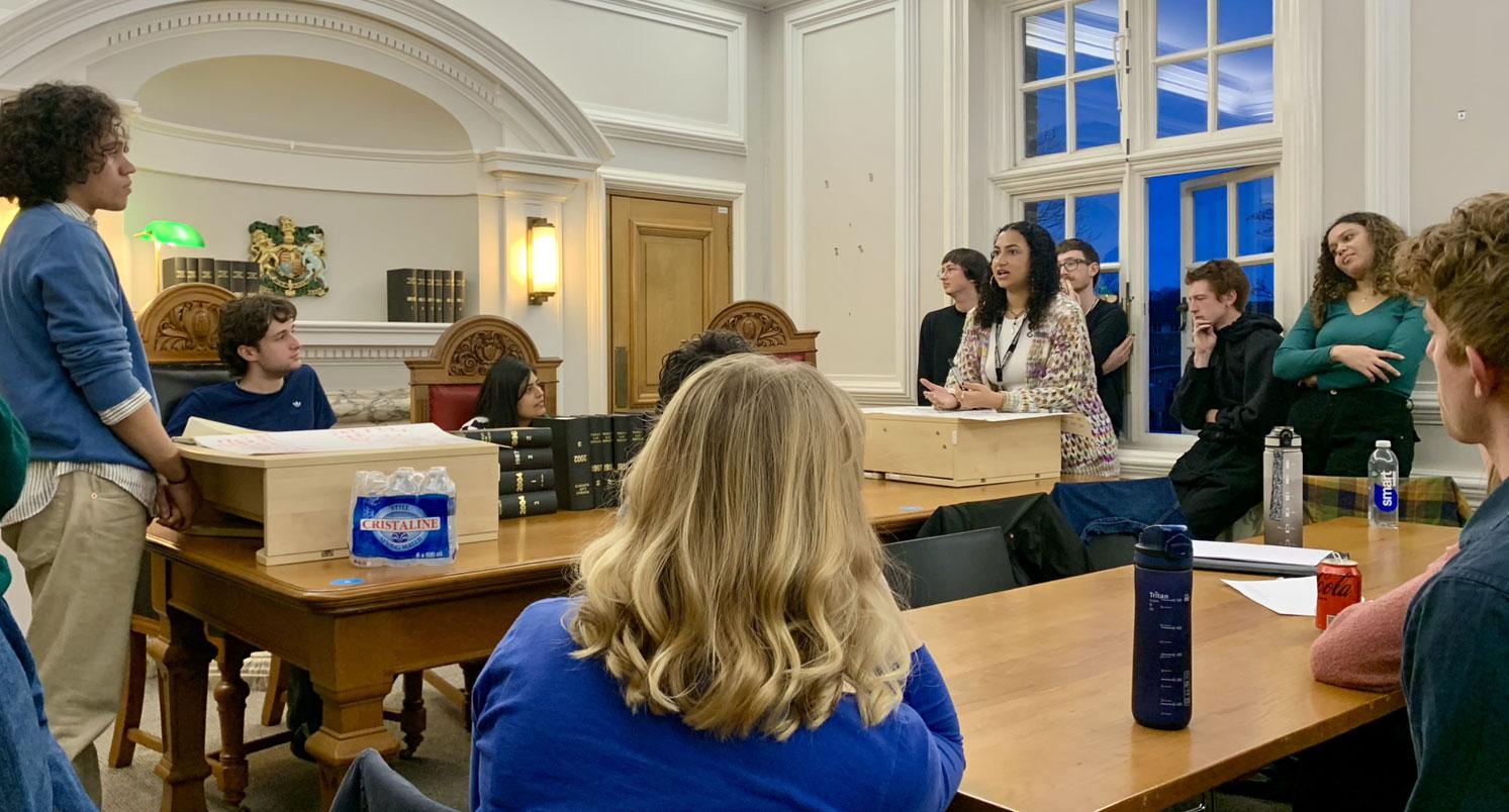 Two students standing across from a table, debating in front of a student audience