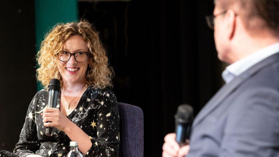 Dr Oonagh Murphy holding a microphone as she sits on stage being interviewed