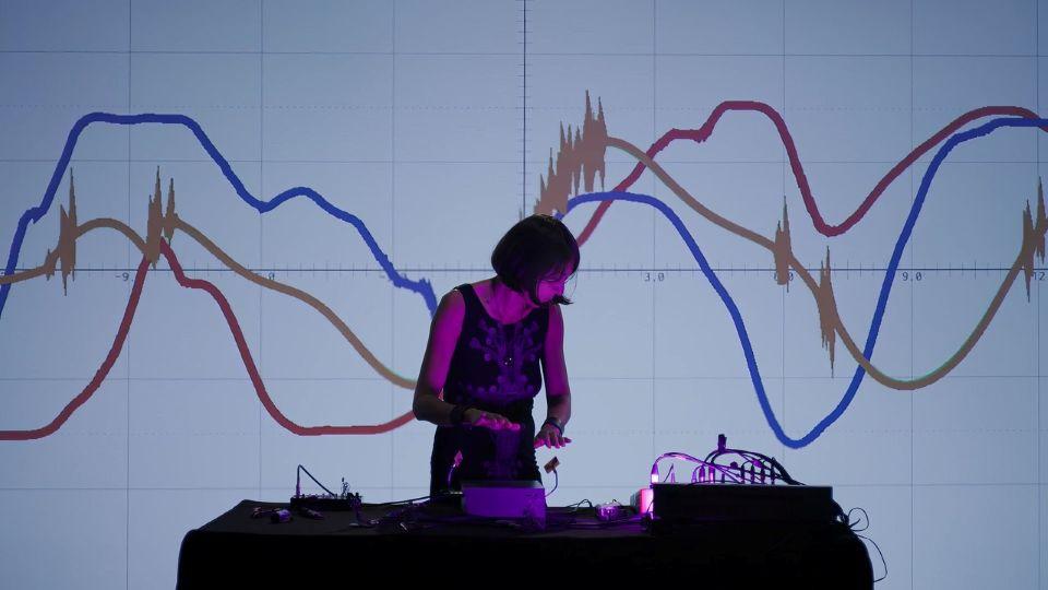 Dr Eleonora Oreggia performing with the REBUS instrument in front of a screen with graphs projected onto it 