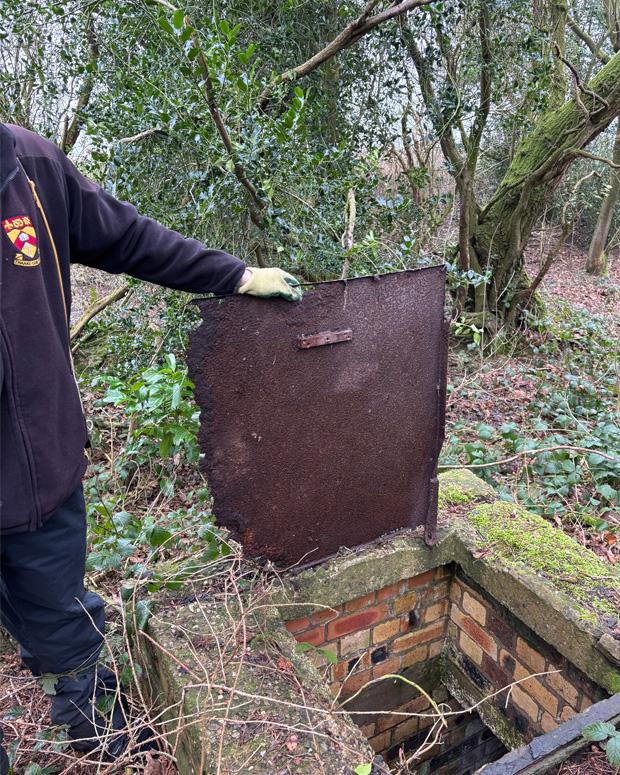 A person holds open an old metal trap door revealing the escape hatch