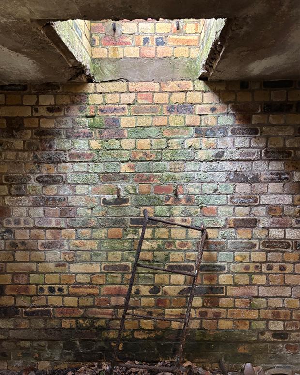 The remains of a ladder lean against the brick wall below the open escape hatch. 