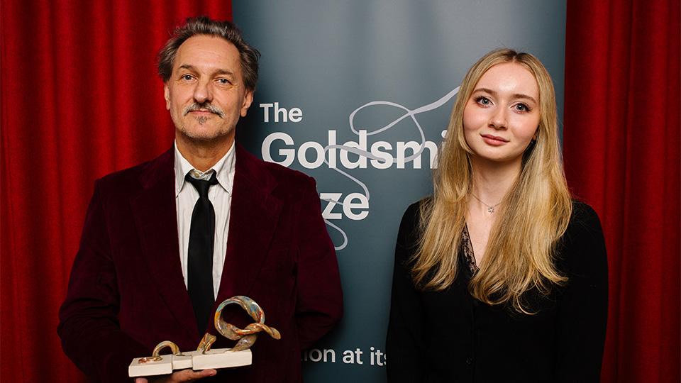 C.D. Rose holding his trophy with Katie Parkinson in front of a banner that says The Goldsmiths Prize