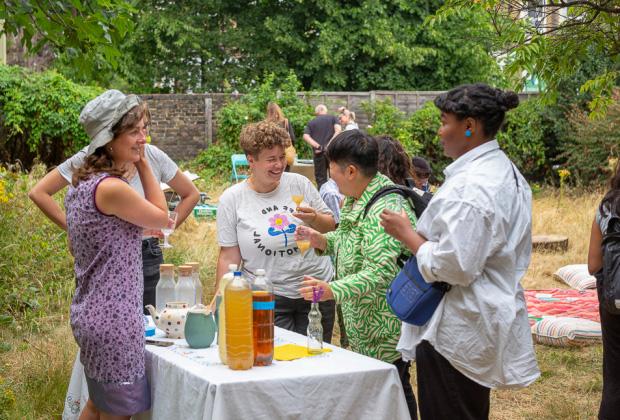 A group of 5 people standing around a refreshment table talking and laughing.
