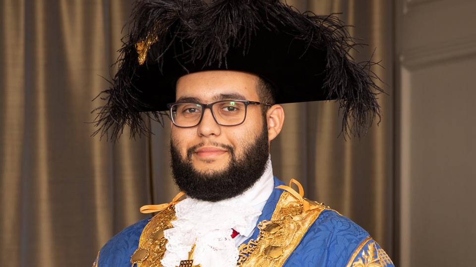 A portrait photograph of Hamza Taouzzale, wearing Mayoral regalia of chain, robe and tricorn hat 
