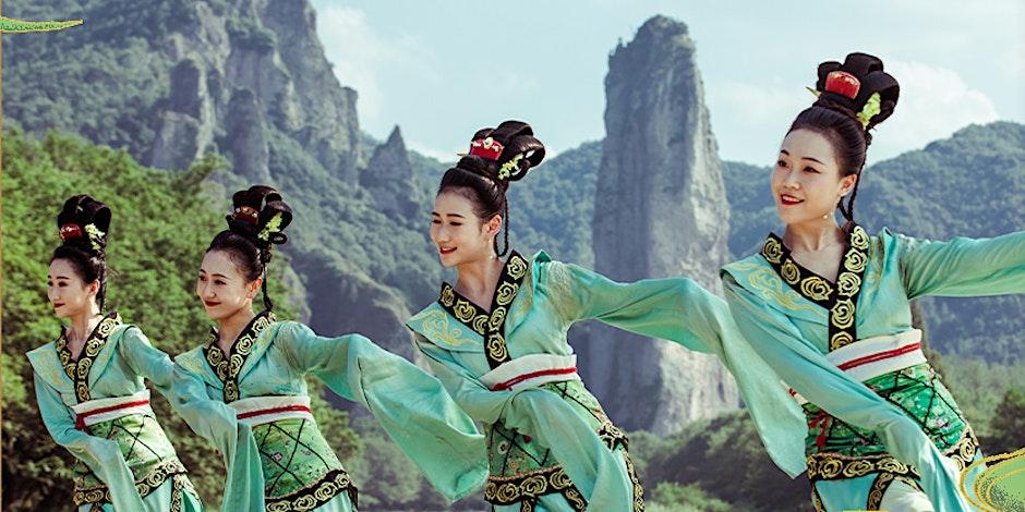 A lady doing a form of chinese dance with a mountain back drop.