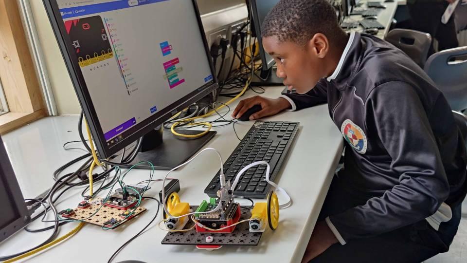 Young boy works at computer with robot to his left