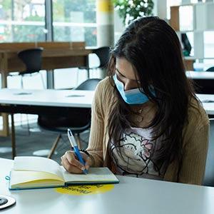Lady sitting in the Library wearing a face covering