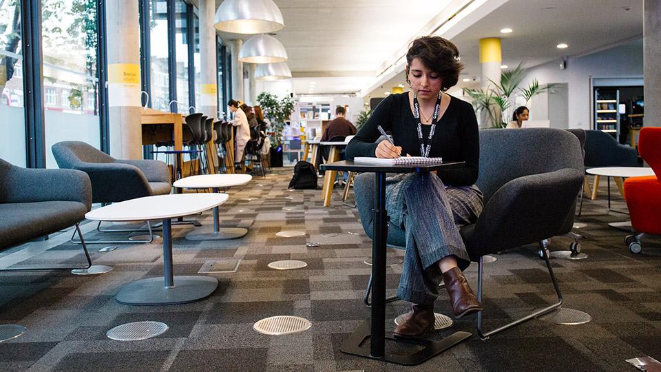 A student writing at a desk in the Library