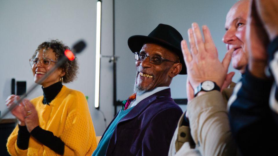 Panelists seated at a long table with microphones and water bottles, as a large projected image fills the backdrop, creating a powerful visual moment during the discussion.