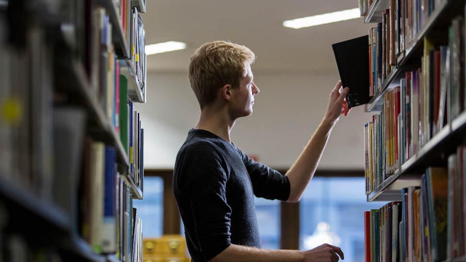 A student in the Goldsmiths library reaching for a book on a high shelf