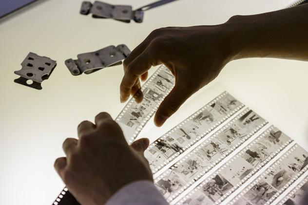 A close-up of two hands holding photography negatives over a lightbox