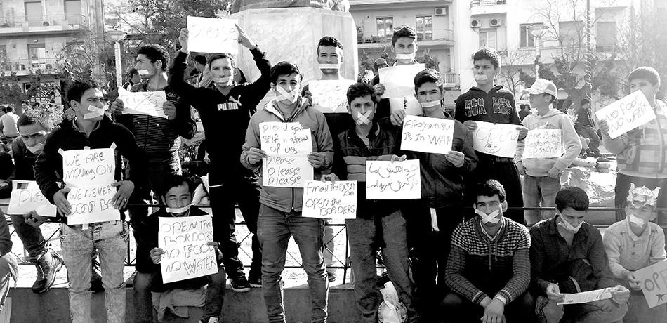 A black and white image of a group of teenage boys, presumably refugees with protest signs and tape around their mouths to symbolize their lost voice.
