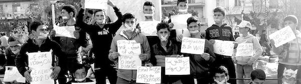 A wide black and white image of a group of men holding placards, they have their mouths taped shut