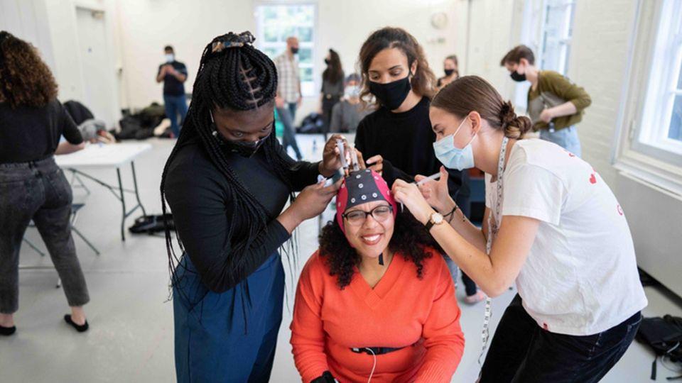 Three people are fitting an EEG cap on a person who is sitting down wearing a red jumper