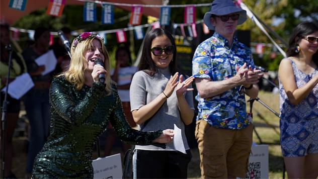 A woman performs spoken word poetry while two people stand and applaud next to her, as part of an outdoor performance