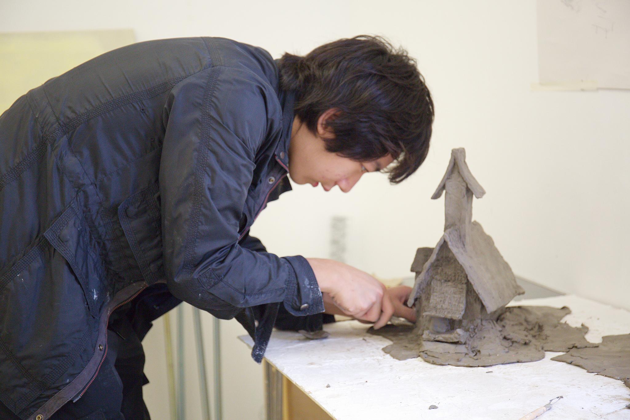 Male student builds intricate grey clay houses as part of the summer school experience.
