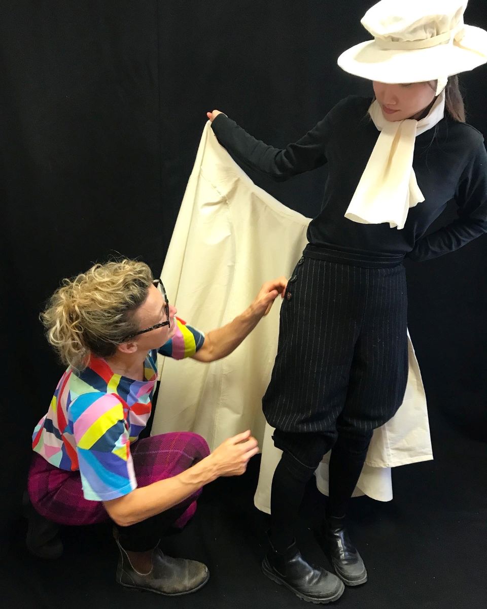 Kat Jungnickel helps a member of the POP team dress in a reconstructed historic sportswear skirt design made from white fabric. 