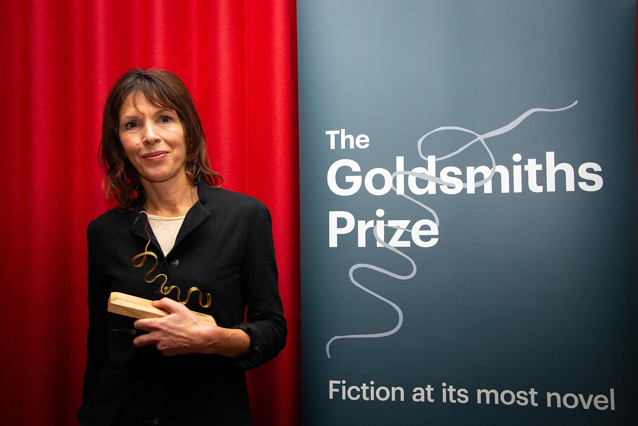 Rachel Cusk standing next to Golddsmith Prize pop up