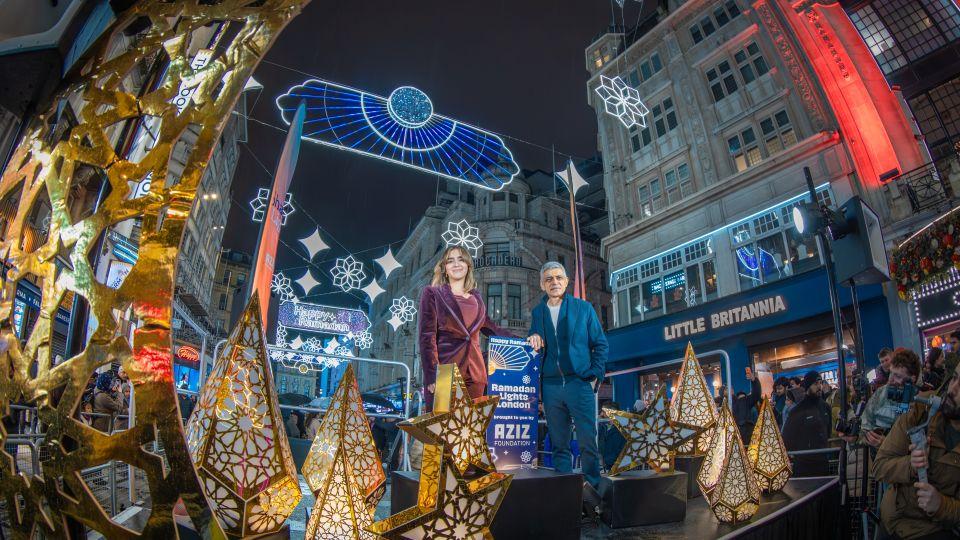 Rahima Aziz and Sadiq Khan standing on a stage decorated with lights underneath the lights display 