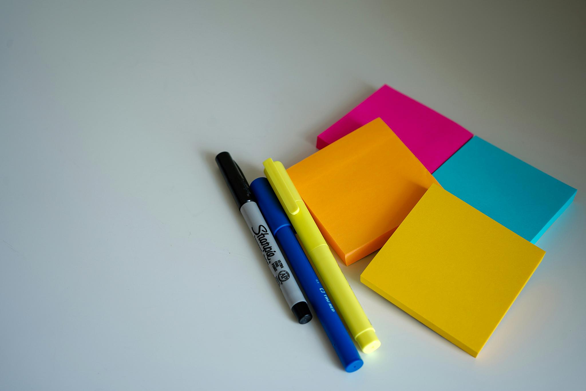 Different coloured sticky notes and pens lying on a surface. 