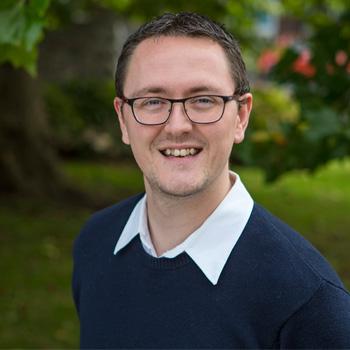 A portrait of a man smiling with bushes and trees in the background