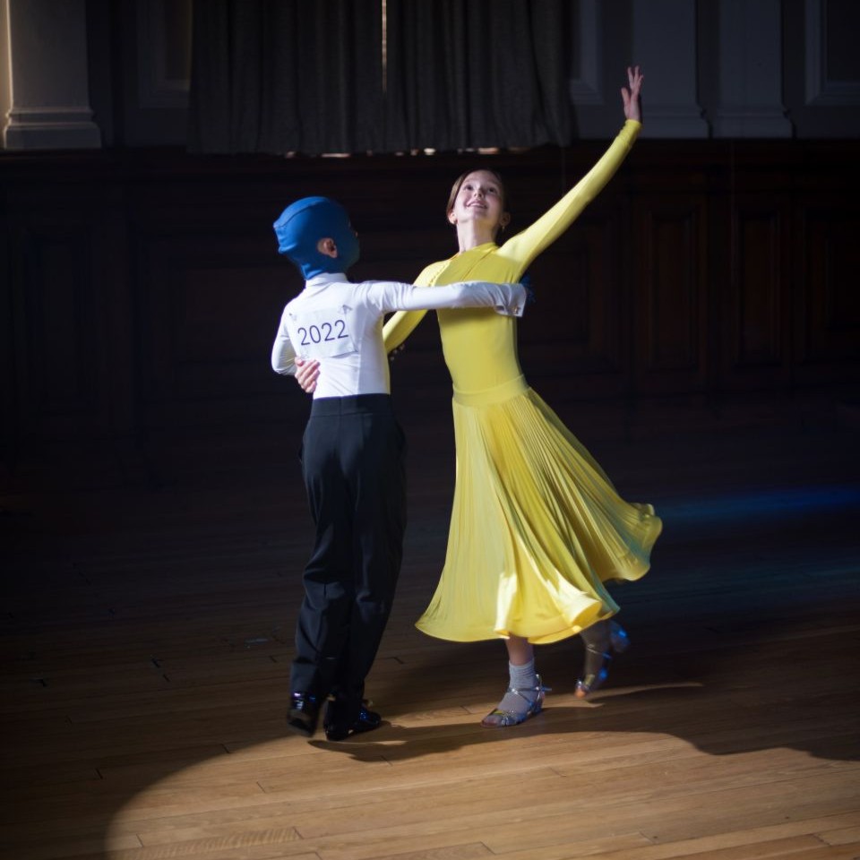 A girl in a yellow dress and a boy wearing a medical mask and formal wear ballroom dancing.