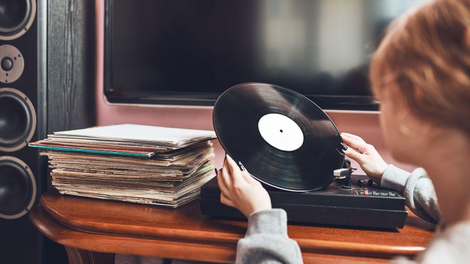Girl holding a vinyl record with a record player and stack of records in the background
