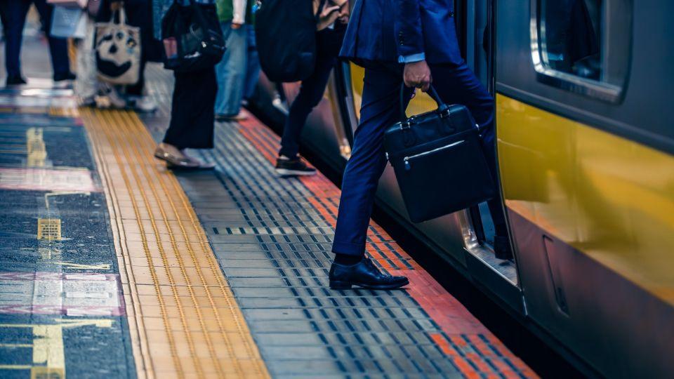 A person wearing a suit and holding a briefcase steps onto a train 