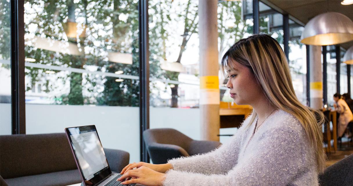 A student works on a laptop in a modern library.