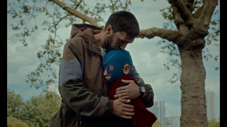 A boy in a blue medical mask being hugged by his father.