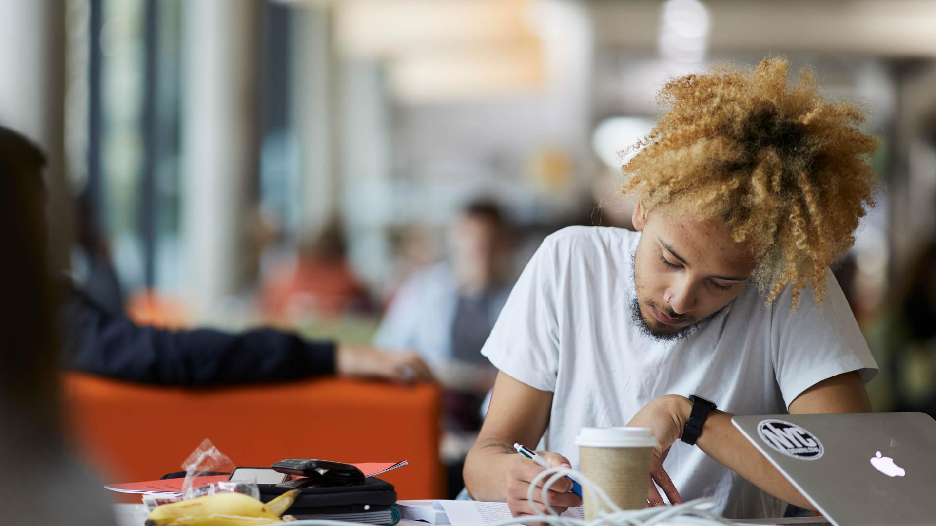 A student in the study space on the ground floor of the library, writing notes in front of a Macbook laptop
