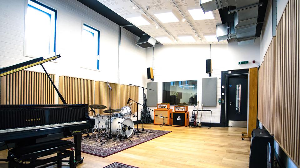 A rehearsal room including a piano, drums and guitars