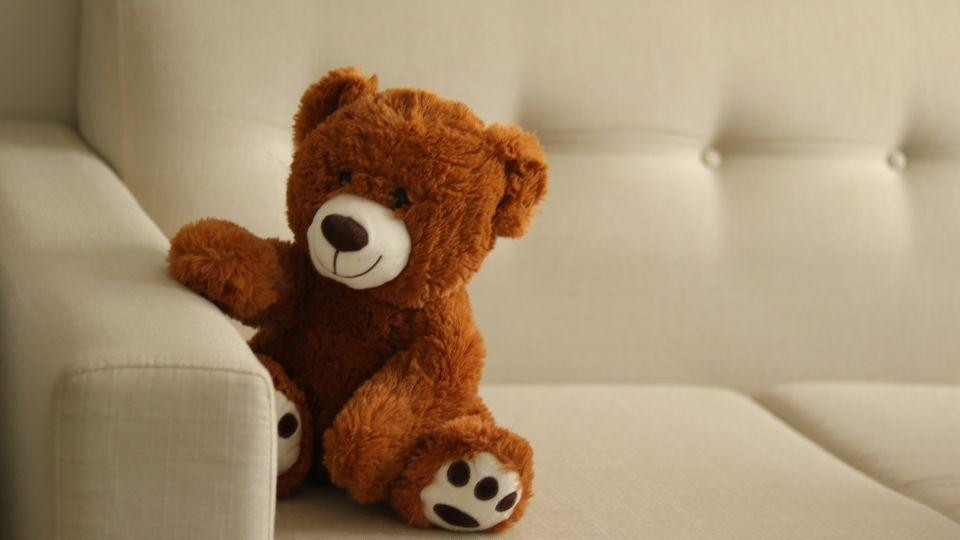 A brown teddy bear on a cream sofa