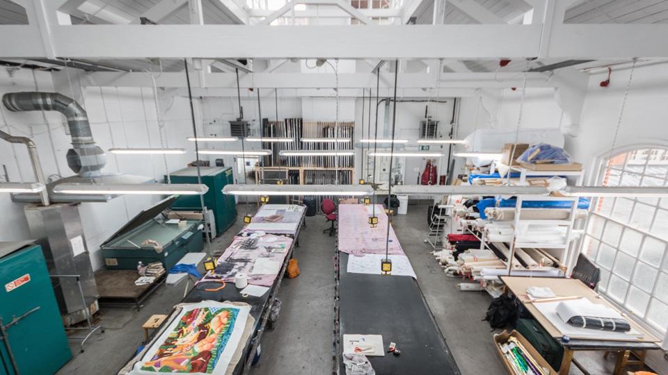 The textiles print and dye art practice area, featuring two long work tables with textiles art work on them, all in a huge white room with a high vaulted ceiling