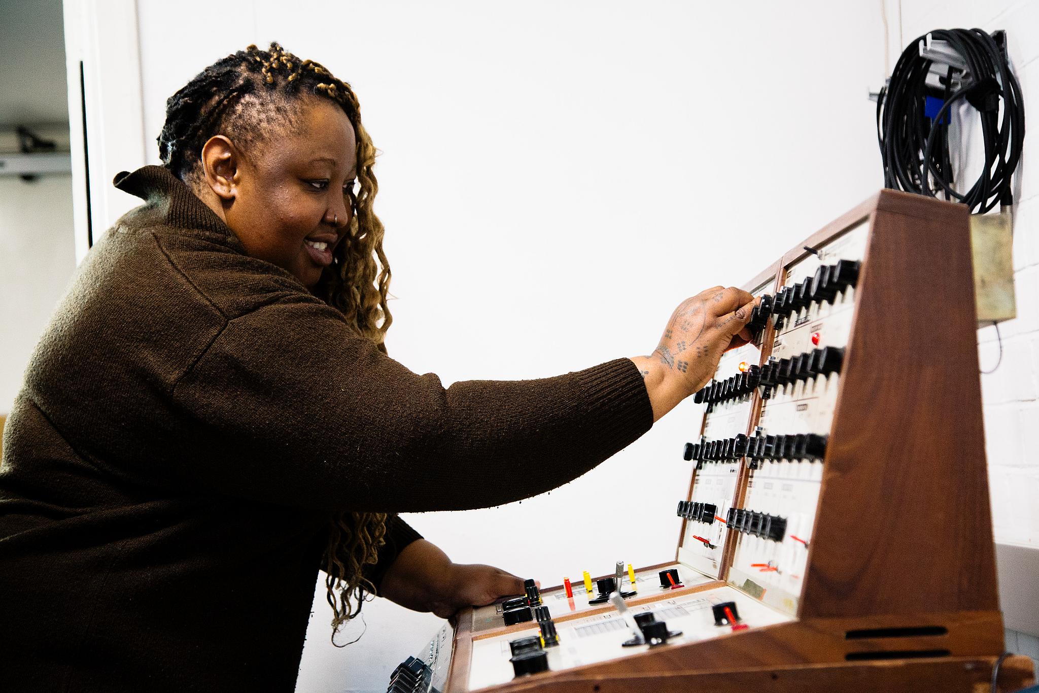 Graduate Trudi Veremu, wearing a brown jumper, plays the VCS4 synthesiser. 