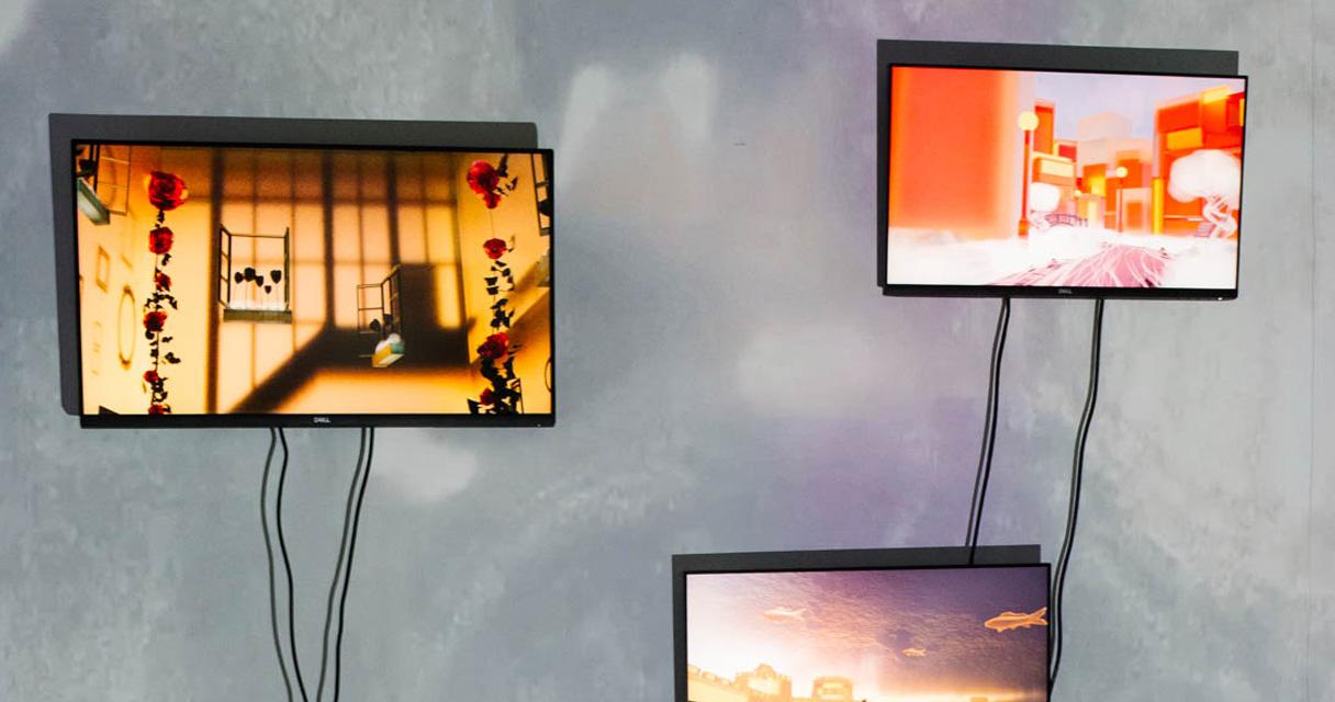 Three screens show colourful images in an exhibition space.