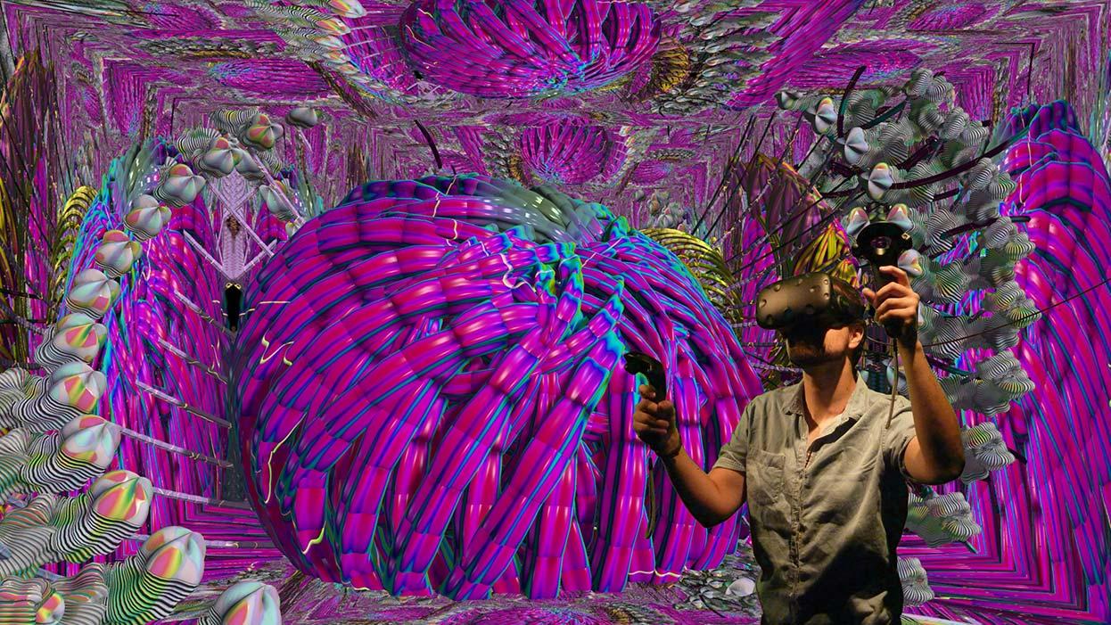 A man in VR headset stands in front of a brightly coloured graphic of curved shapes