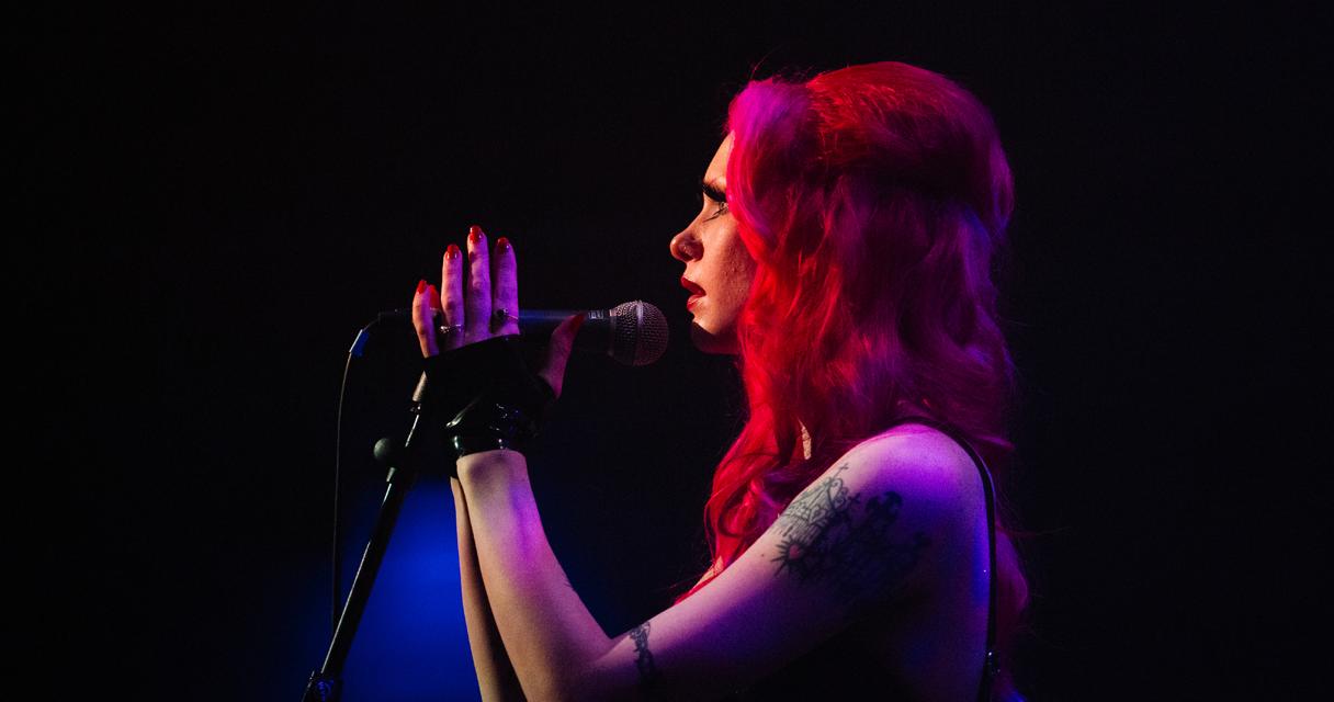 A woman with died red hair and tattoos performs on stage