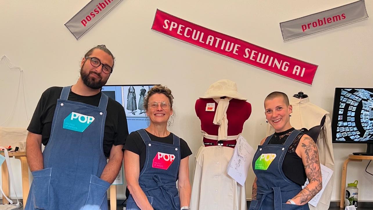 Three people stand in a sewing studio with a mannequin and a banner which reads Speculative Sewing AI